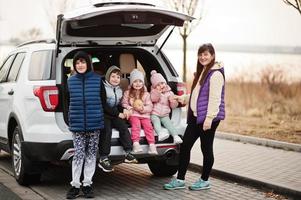 madre con quattro bambini seduti nel bagagliaio di una grande auto suv. foto