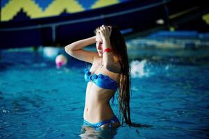 ritratto di una giovane ragazza attraente in piedi e in posa in piscina indossando bikini blu nel parco acquatico. foto