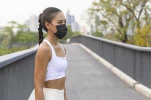 giovane donna fitness in abbigliamento sportivo che indossa la maschera durante l'esercizio nel parco cittadino, salute e stili di vita. foto