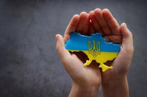 mani che tengono la forma del confine dell'Ucraina con la bandiera a colori foto