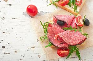 panino con salsiccia, olive, pomodoro e rucola sullo sfondo di legno vecchio foto