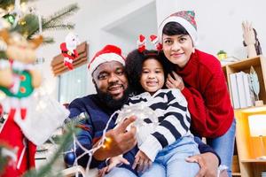 la famiglia afroamericana aiuta a decorare l'albero di natale a casa. buon Natale. foto