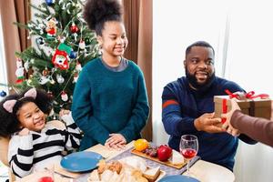 famiglia afroamericana che sorprende insieme a un regalo il giorno di natale durante la cena. foto