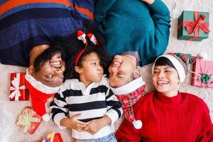 famiglia afroamericana in tema natalizio. felice famiglia afroamericana di quattro persone che si legano insieme sul pavimento. foto