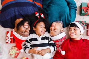 famiglia afroamericana in tema natalizio. felice famiglia afroamericana di quattro persone che si legano insieme sul pavimento. foto