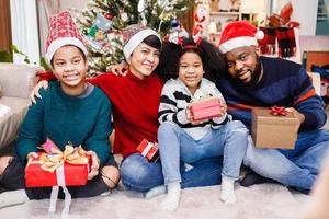 famiglia afroamericana in tema natalizio. felice famiglia afroamericana di quattro persone che si uniscono insieme sul pavimento foto