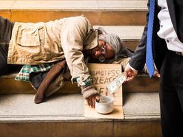 un uomo d'affari dà soldi a un senzatetto che dorme su una scala foto