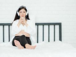 bella donna incinta ascolta musica dalle cuffie e beve latte di soia per una buona salute foto