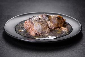 sardine in scatola sott'olio su un piatto rotondo nero su uno sfondo di cemento scuro foto