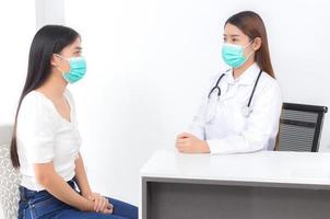 la dottoressa asiatica sta parlando con una paziente in ospedale, entrambe indossano una maschera medica per proteggere il microrganismo patogeno nel sistema respiratorio. foto