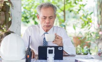 uomo d'affari o ingegnere che legge tablet pc mentre beve caffè, anziani asiatici foto