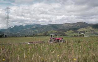 trattore rosso che ara un campo con erba verde durante una giornata con cielo nuvoloso foto