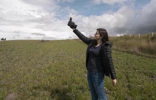 bella blogger ispanica che si filma con la sua macchina fotografica in mano felice in posa in mezzo al campo foto