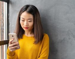 seria, premurosa bella giovane donna asiatica che guarda il telefono cellulare, leggendo i messaggi foto