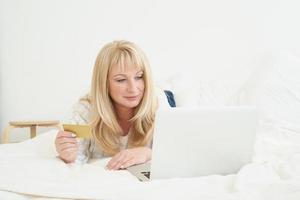 femmina di mezza età sullo shopping online. la bella donna bionda matura sta tenendo la carta di credito foto