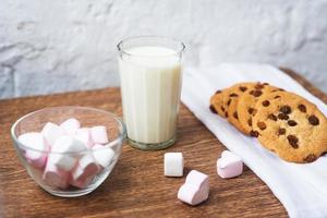 biscotti fragranti, gustosi, fatti in casa con uvetta, marshmallow a forma di cuori e bicchiere di latte fresco in tavola foto