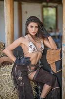 sensuale donna bruna con look sexy country. ritratto di una ragazza con lingerie brow, pantaloni in pelle da cowboy e guanti. ragazza che interagisce e si diverte al ranch. stile country sexy americano foto