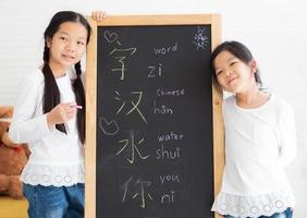 due bambini piccoli in piedi vicino alla lavagna felice di scrivere il testo cinese. i giovani fratelli asiatici studiano insieme a casa imparando facilmente la lingua cinese, scrivono sulla lavagna. stile di vita dei bambini di homeschooling. foto