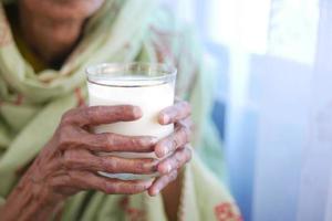 mano delle donne anziane che tiene un bicchiere di latte foto