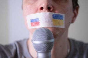 una bocca con del nastro adesivo con una bandiera della russia e dell'ucraina che cerca di parlare in un microfono. foto