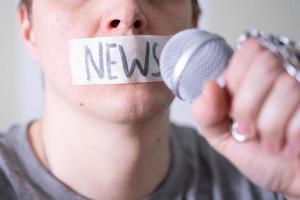 un uomo si imbavaglia la bocca con del nastro adesivo dicendo notizie cercando di parlare in un microfono. foto
