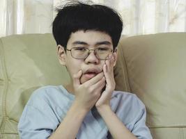 il ragazzino asiatico soffre di mal di denti. è triste con dolore ai denti, malattie dentali, bambino che soffre di problemi dentali. pianificare un appuntamento dal dentista. foto