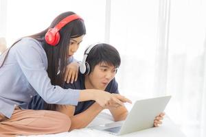 una felice giovane coppia asiatica è seduta a letto e si diverte a guardare film su un laptop su uno sfondo bianco. foto