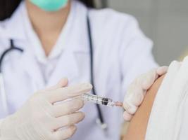 un primo piano della mano di una dottoressa che usa una siringa e cotone per vaccinare un paziente, una mano guantata che tiene una siringa per vaccinare. foto