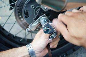 primo piano mano dell'operaio tecnico, ruota della moto fissa all'esterno del garage. foto