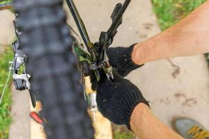 l'uomo meccanico della bici ripara la bicicletta nell'officina di riparazione della bicicletta, all'aperto. la mano del ciclista il ciclista esamina, ripara il moderno sistema di trasmissione del ciclo. manutenzione della bici, concetto di negozio di articoli sportivi. foto