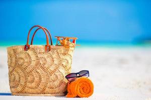 accessori da spiaggia - aeroplanino giocattolo, borsa di paglia, asciugamano arancione e occhiali da sole sulla spiaggia foto
