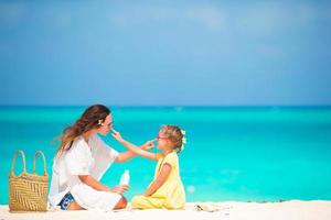 bambina adorabile che applica crema solare al naso della madre foto