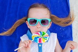 primo piano adorabile bambina con lecca-lecca sulla spiaggia tropicale foto