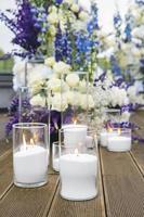 primo piano di candele bianche al ricevimento di nozze con fiori bianchi, blu e viola, all'aperto. elegante composizione di decorazione di nozze di lusso sul luogo della cerimonia foto