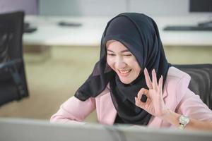 felice donna musulmana sorridente in hijab che mostra gesticolando segno ok, allegra donna d'affari musulmana che fa segno ok con la mano e le dita in ufficio foto