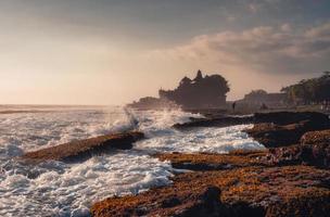 tempio di pura tanah lot sulla cima di una scogliera e onde che si infrangono sulla spiaggia al tramonto a bali foto