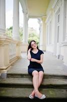 ragazza bruna in abito nero, occhiali da sole seduti sulle scale della vecchia casa d'epoca, in posa in una strada della città. foto