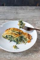 porzione di pasta sfoglia al formaggio e spinaci affettati su un piatto con forchetta foto