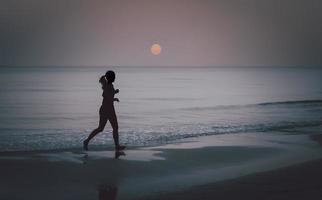 silhouette di donna a piedi nudi che corre sulla spiaggia all'alba. foto