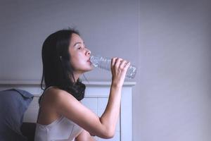 la donna si sveglia al mattino seduta a letto bevendo acqua minerale dalla bottiglia. foto