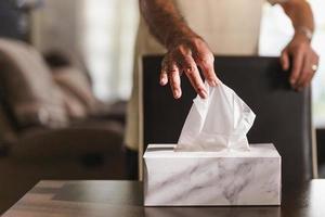 mano dell'uomo anziano che raccoglie la carta velina dalla scatola del tessuto sul tavolo da pranzo. foto