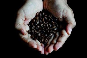 chicchi di caffè nelle mani del cuore a forma di su tavola di legno in stile scuro foto
