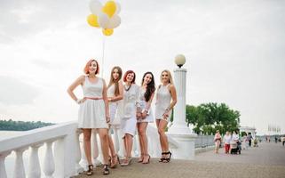 cinque ragazze con palloncini a portata di mano indossate su abiti bianchi su addio al nubilato contro il molo sul lago. foto