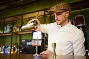 barman versando un cocktail nel bicchiere in un pub moderno foto