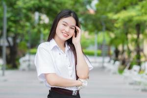 giovane studentessa asiatica che ha i capelli lunghi biondi sorride e guarda alla telecamera mentre si tiene per mano e in piedi all'università con lo sfondo dell'albero del giardino all'aperto. foto