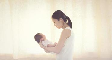 bambino asiatico di due giorni nel comfort delle braccia della mamma, neonato foto