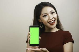 giovane donna asiatica felice e sorridente che mostra e che indica uno schermo vuoto verde. foto