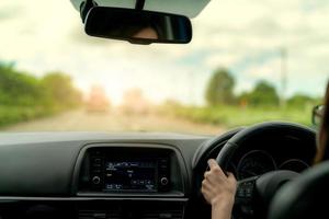 vista posteriore di una donna che guida un'auto per un viaggio estivo su strada. guida in auto con sicurezza su strada asfaltata. volante che tiene la mano del conducente per l'auto di controllo. vista interna dell'auto. cruscotto e parabrezza. foto