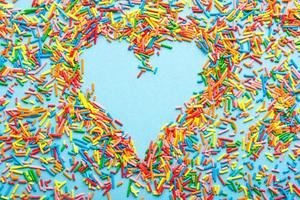 flatlay di concetto semplice con un cuore fatto di granelli di zucchero colorati. foto