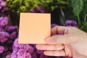 carta per appunti vuota in mano sul bellissimo sfondo viola del bouquet di fiori di margaret, copia-spazio sulla carta per inserire il tuo messaggio. foto